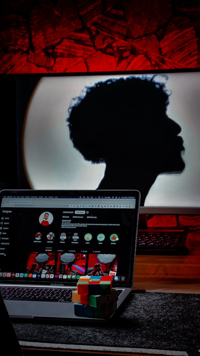 Silhouette of person behind laptop with Rubiks cube on desk, modern studio setup.