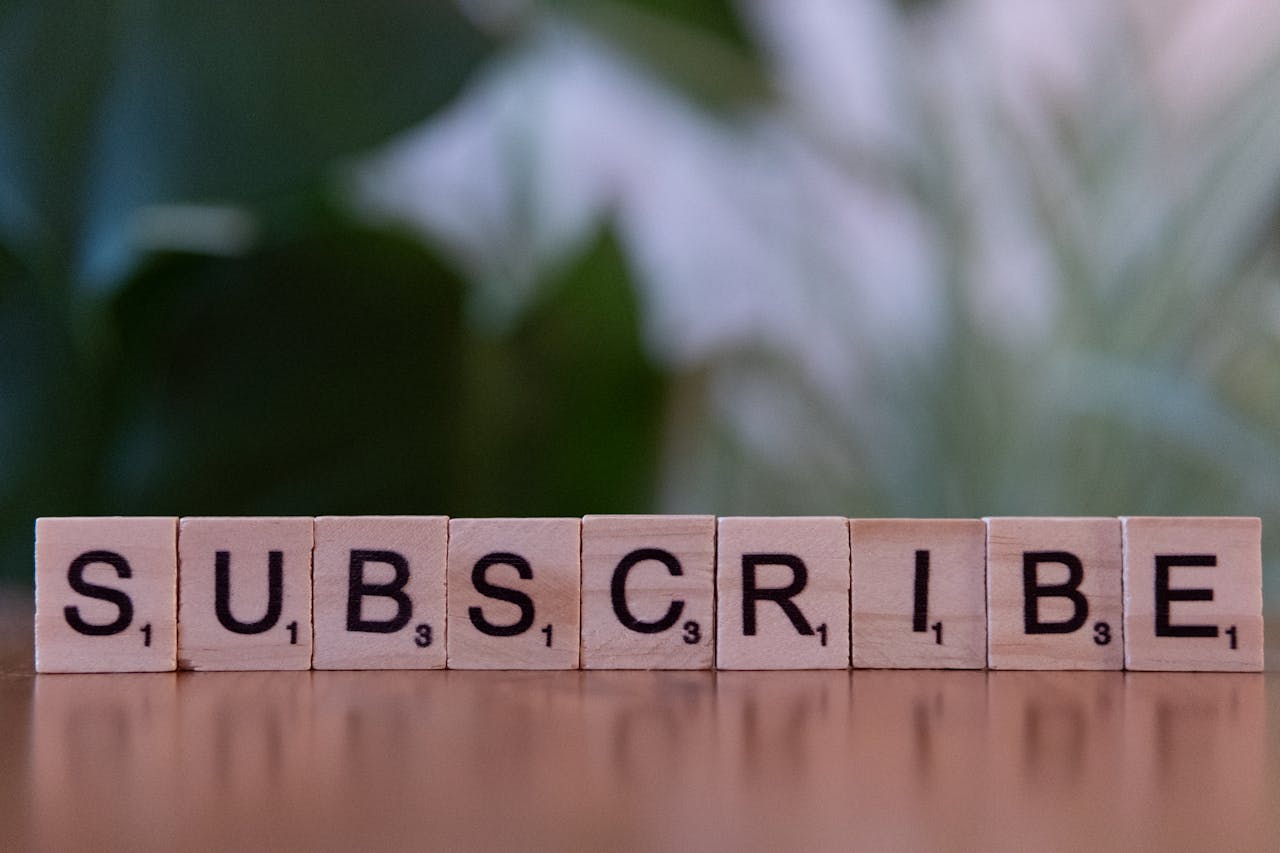 services-01 Close-up of the word SUBSCRIBE spelled with wooden letter tiles on a table.